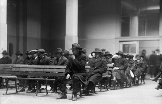 Men in overcoats and hats sit on rows of benches.