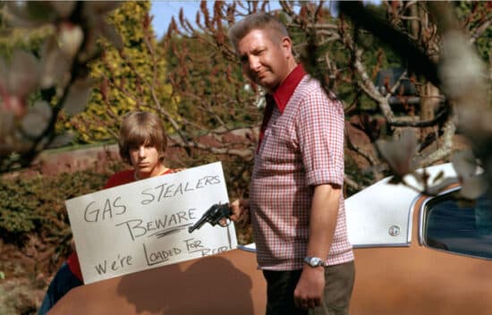 A man holds a gun and a boy holds a sign that reads, Gas Stealers Beware. We're Loaded For Bear.