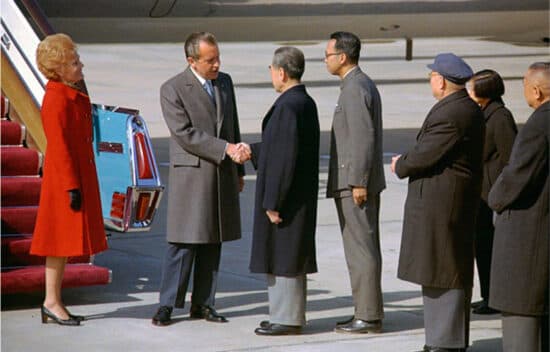 President Nixon and Premier Zhou Enlai shake hands in front of an airplane staircase. Nixon's wife, Pat, and Chinese leaders look on.