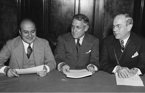 R.E. Desvernine, Jouett Schouse, and Earl F. Reed sit side-by-side at a table and hold papers.