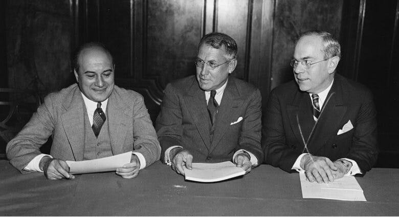 R.E. Desvernine, Jouett Schouse, and Earl F. Reed sit side-by-side at a table and hold papers.