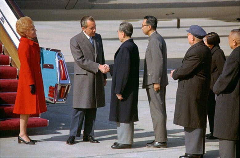 President Nixon and Premier Zhou Enlai shake hands in front of an airplane staircase. Nixon's wife, Pat, and Chinese leaders look on.