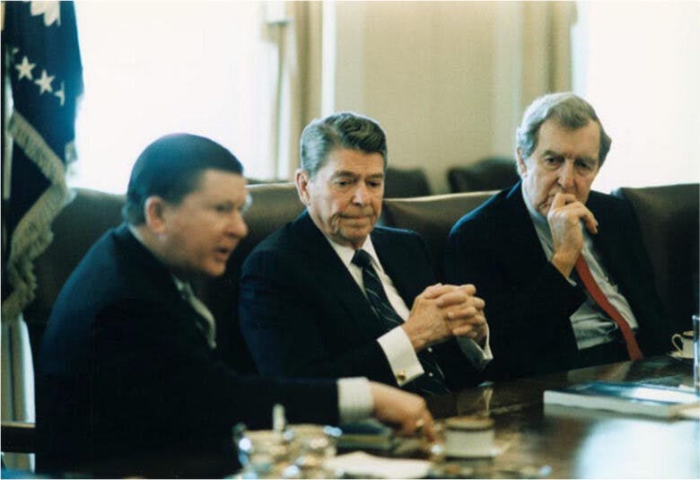 President Ronald Reagan sits at a table between Edmund Muskie and John Tower.